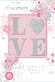 This anniversary card unfolds like a quiet love story, the design capturing the gentle intimacy of a shared life in Hounslow. The centrepiece is the word LOVE, crafted in softly raised glitter so that each letter offers a pleasing texture under the fingertips. The 'O' is transformed into a shimmering silver heart, subtly textured to reflect the light with a delicate sparkle much like dewdrops on early-morning blooms in Lampton Park. The letters rest against a pastel pink background that feels tender and calm, creating an immediate sense of warmth. Flowing out from this focal word, an array of illustrated blossoms in blush, soft mauve, and muted ivory unfurl with a watercolour softness, their edges delicately defined with fine lines and gentle shading. Slim vines and swirling flourishes curl around the flowers, adding a sense of grace and movement, evoking the feel of an English spring garden just after a light rain. Tiny, almost-whispered details-floating petals, slender curls, and small butterfly motifs-add a playful, whimsical note without disturbing the card's serenity. The anniversary text, including phrases such as On Our Anniversary and I love you today and always, appears in an elegant, flowing script that feels personal, as though carefully written for someone waiting at home near Hounslow Central. The overall impression is of a lovingly composed keepsake: soft-spoken yet deeply heartfelt, like a hand-tied anniversary bouquet translated into paper, ready to be given alongside fresh flowers delivered across the local area.